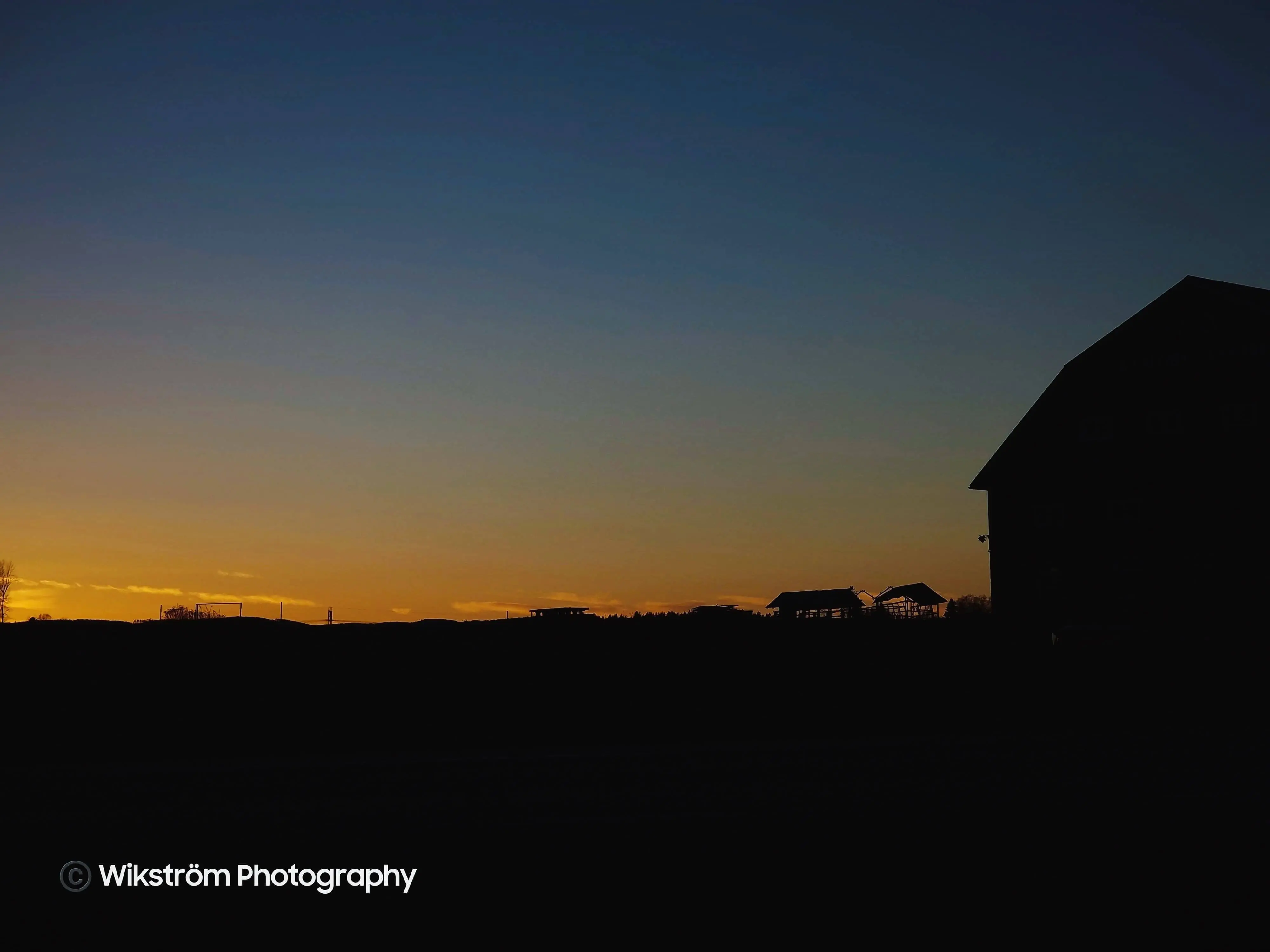 A siluett of a barn and a field during sunset.